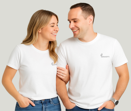 Smiling couple standing side by side wearing matching white unisex t-shirts and jeans, in front of a soft gray backdrop.